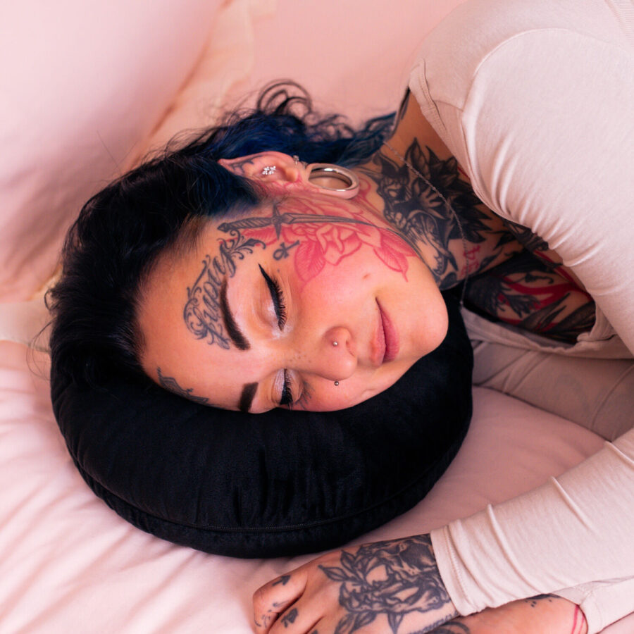 Persona con tatuaggi sdraiata su un cuscino da piercing nero su biancheria da letto rosa
