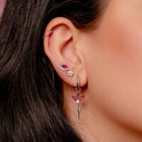 Orecchino d'argento all'orecchio con cristalli rossi e diversi piercing in un orecchio