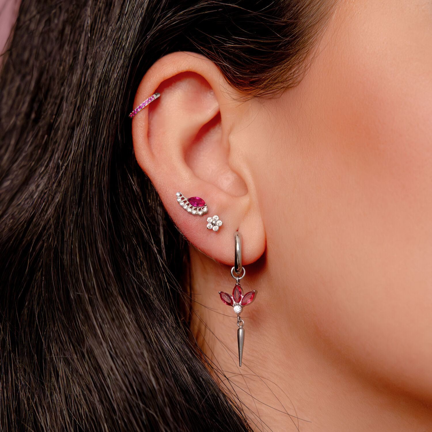 Orecchino d'argento all'orecchio con cristalli rossi e diversi piercing in un orecchio