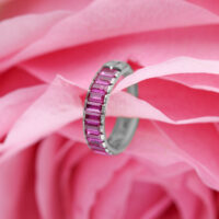 Anello piercing argento con cristalli baguette rossi su sfondo di fiori rosa