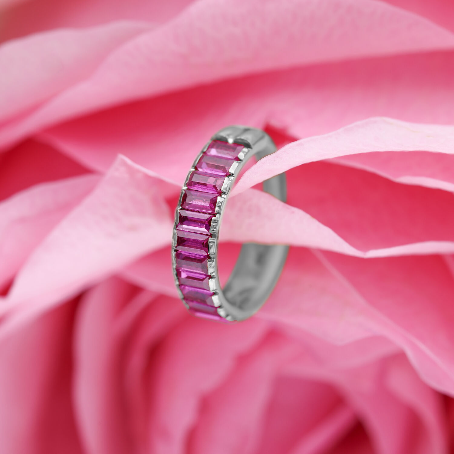 Anello piercing argento con cristalli baguette rossi su sfondo di fiori rosa
