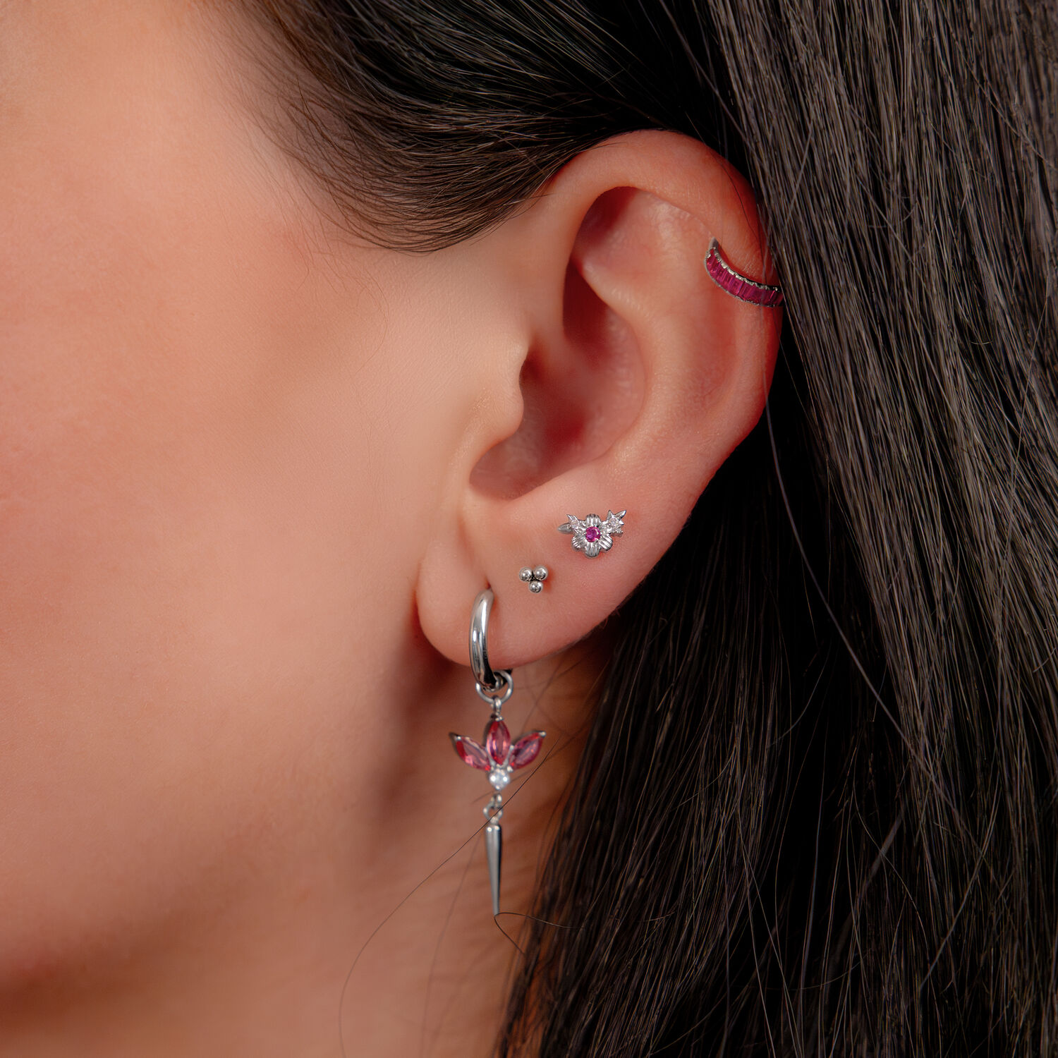 Orecchio con più piercing, incluso un clicker argento con cristalli rossi.