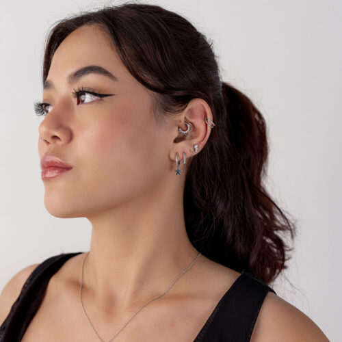 Donna con capelli scuri indossa un septum clicker nero e diversi orecchini di varie forme su sfondo bianco.