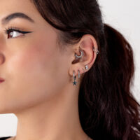 Primo piano di un orecchio con diversi piercing in argento, incluso un ciondolo a stella, su sfondo bianco