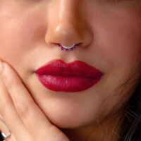 Primo piano di un viso con piercing al setto in argento e cristalli rossi