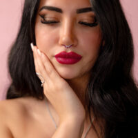 Donna con capelli neri e piercing al naso in argento con cristallo rosso su sfondo rosa