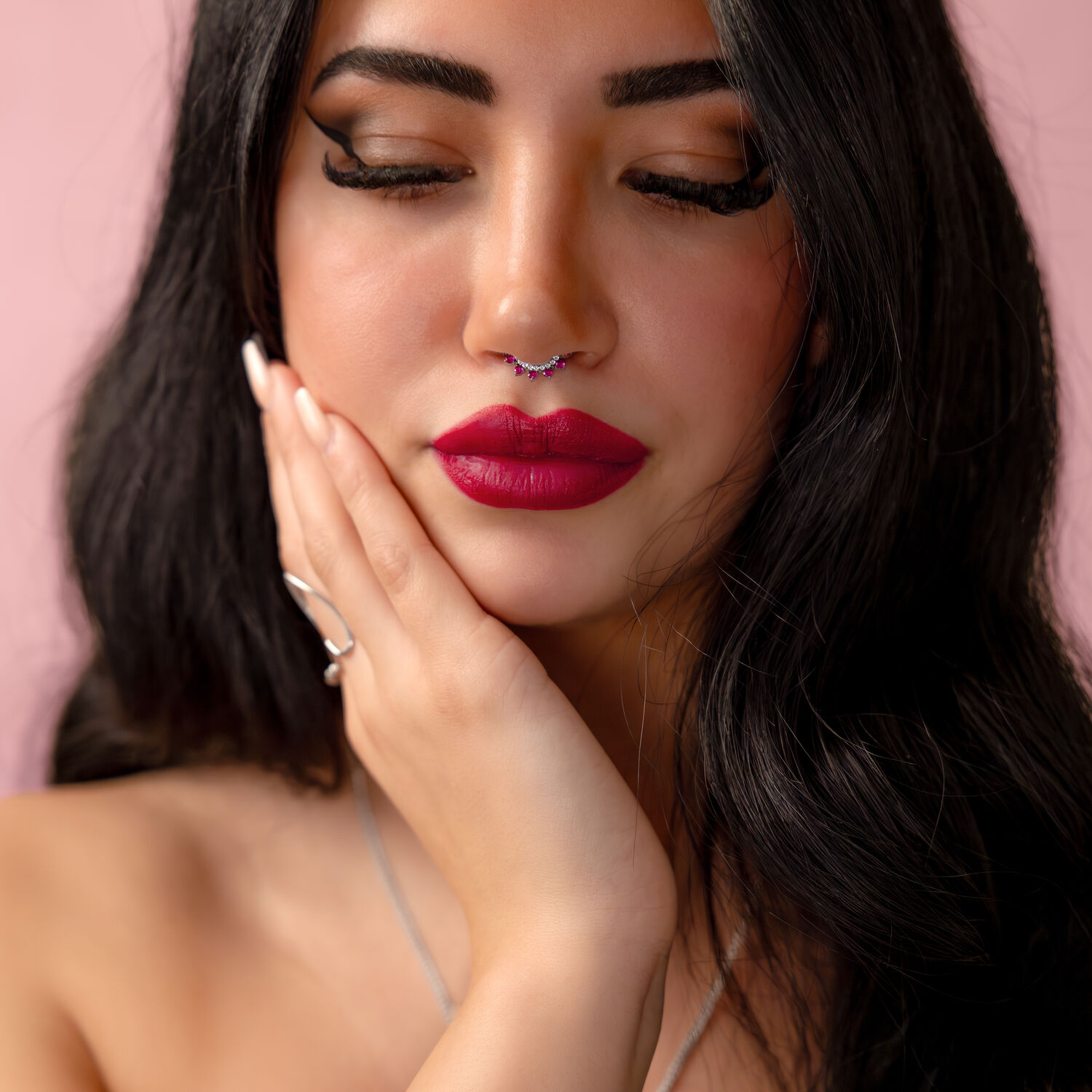 Donna con capelli neri e piercing al naso in argento con cristallo rosso su sfondo rosa