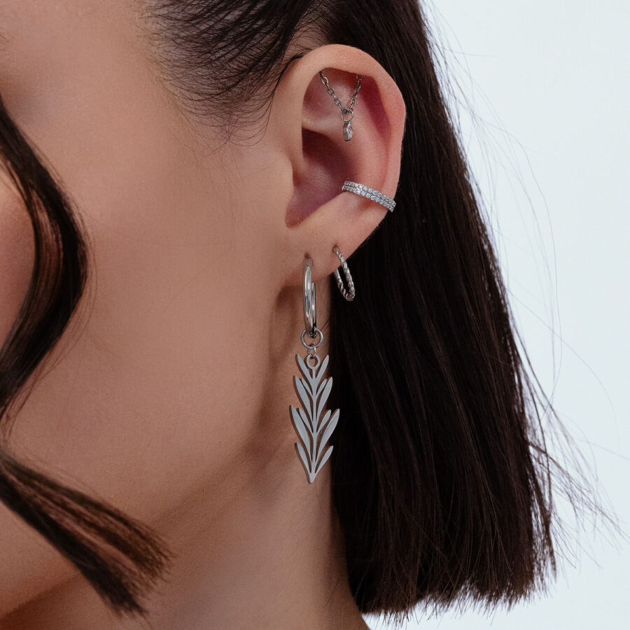 Primo piano di un orecchio con orecchini in argento a forma di foglia, diversi piercing