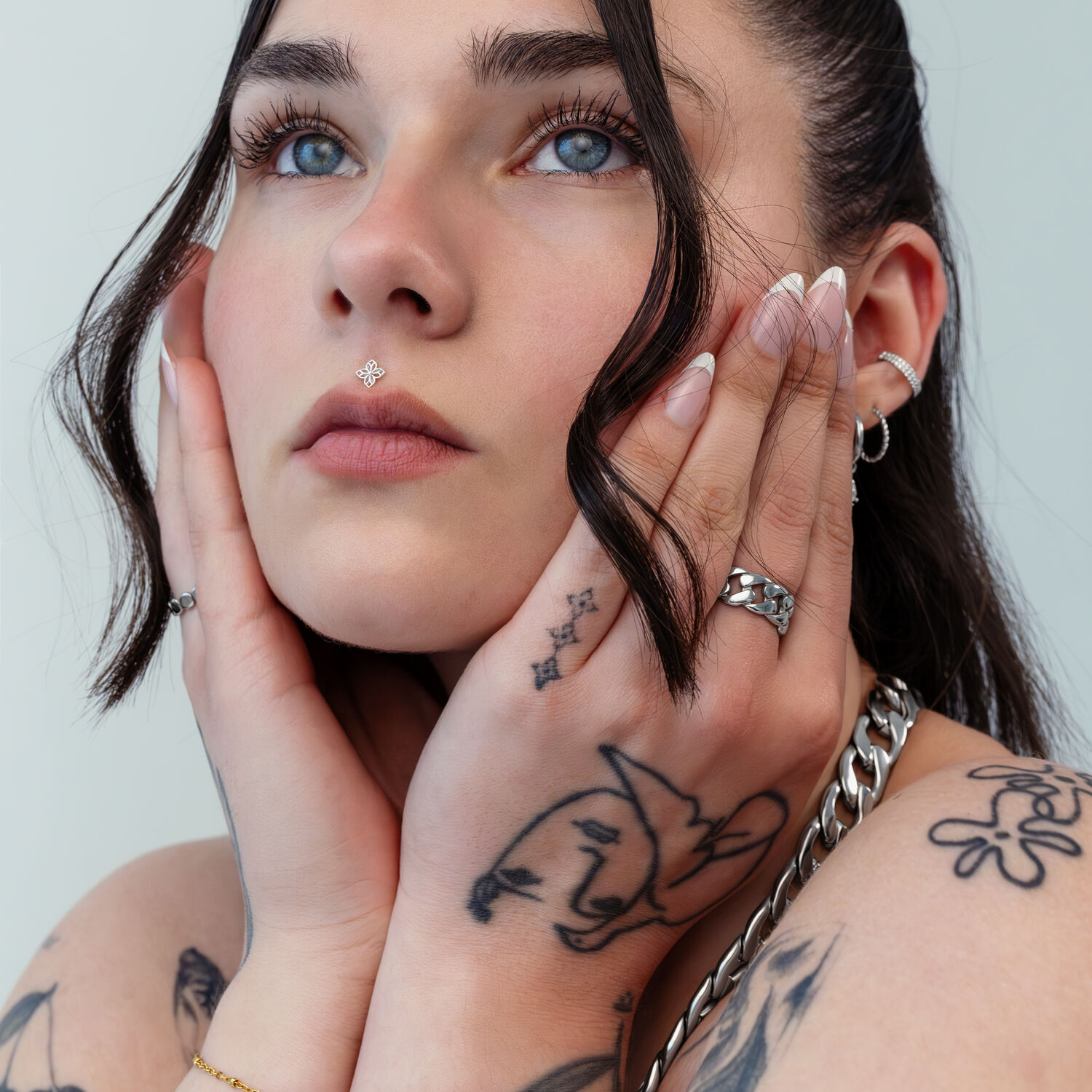 Inserto floreale Push Fit argento Donna con mani tatuate che toccano il viso, indossa un inserto floreale argento nel piercing al naso