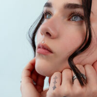 Push Fit Fiore in Argento Primo piano di un viso con un piercing al naso a forma di fiore in argento, sfondo azzurro