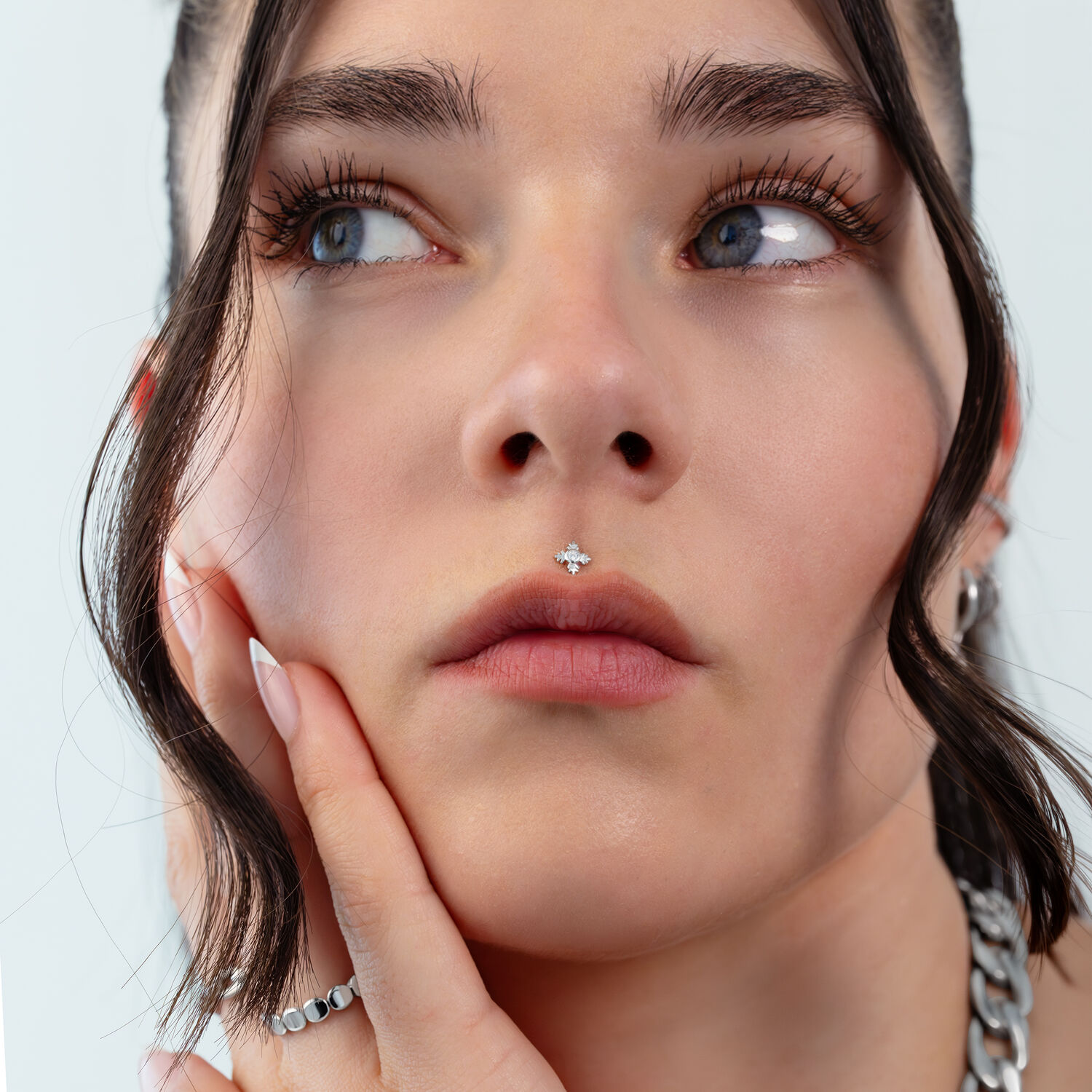 Primo piano di un viso con piercing a foglia d'argento al naso, capelli sullo sfondo