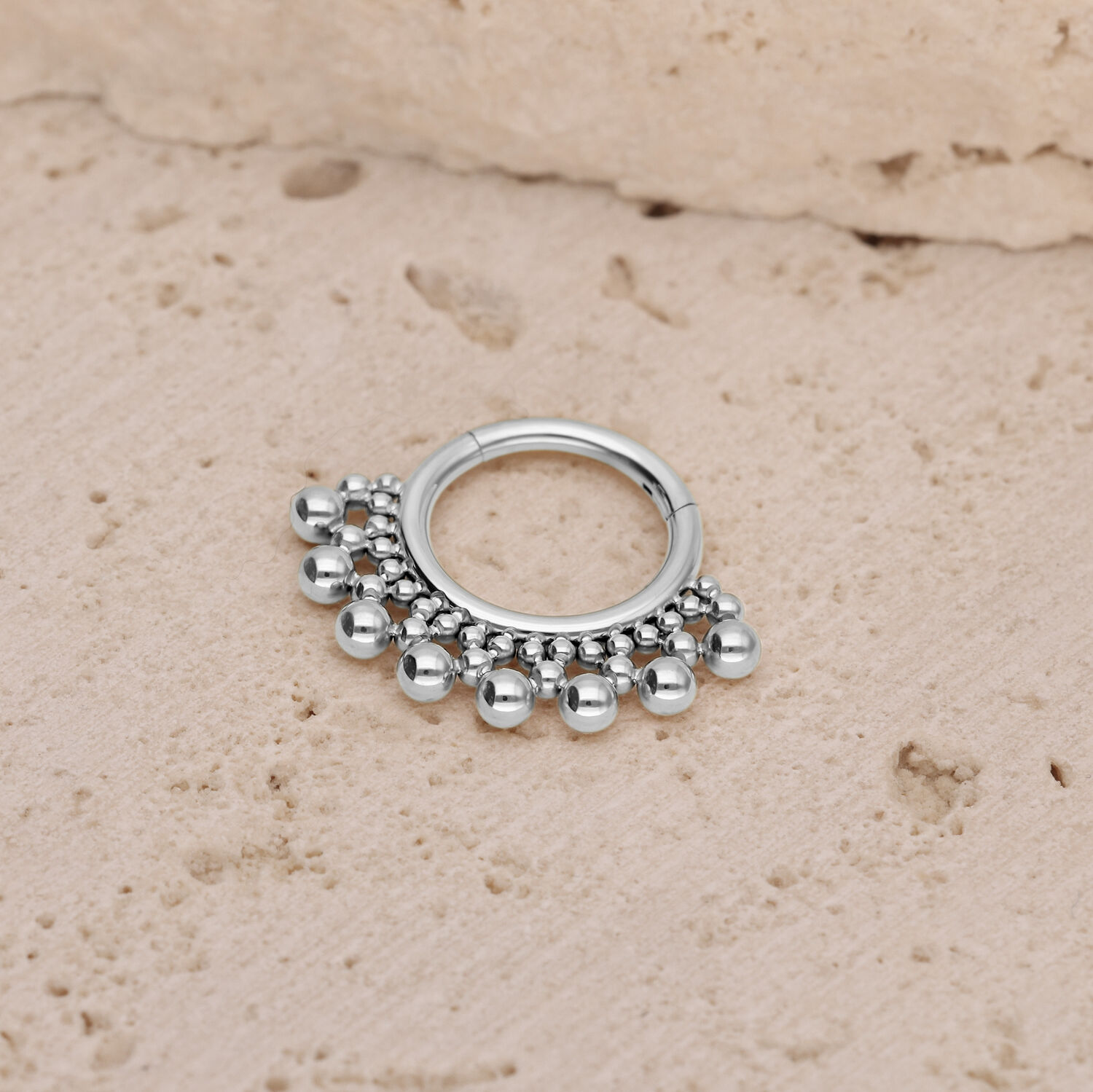 Clicker per setto in titanio argento con sfere Clicker per setto argento con piccole sfere su sfondo di pietra strutturata