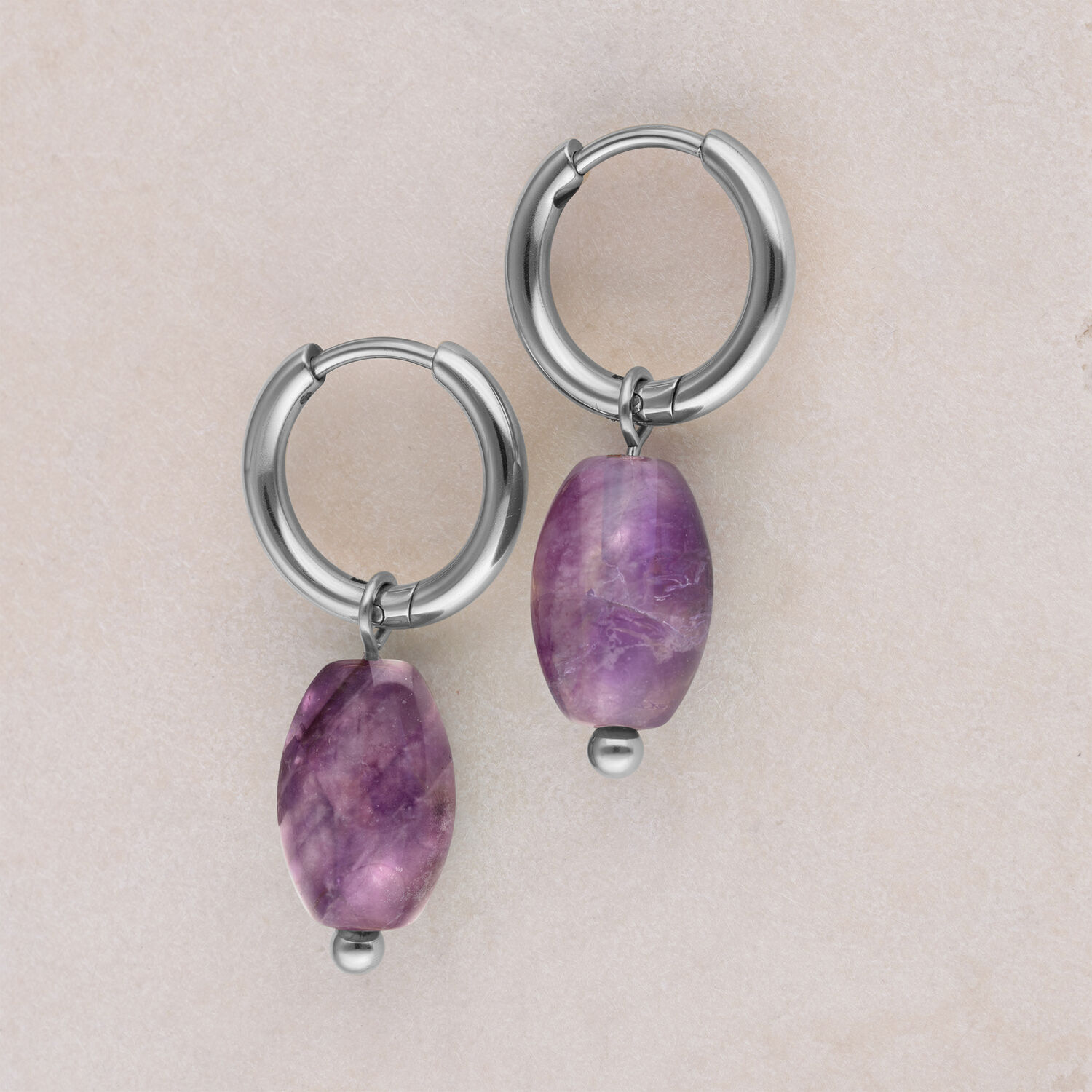 Due orecchini a cerchio in argento con pendente di ametista viola su sfondo beige