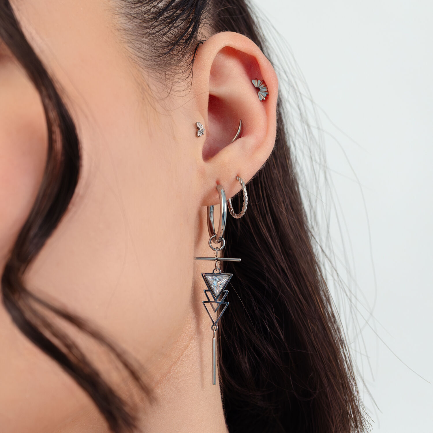 Donna con orecchini Art Deco argento e diversi piercing all'orecchio su sfondo bianco