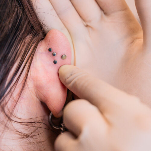 Primo piano di un orecchio con tre labret piercing neri e un dito che tocca i piercing.