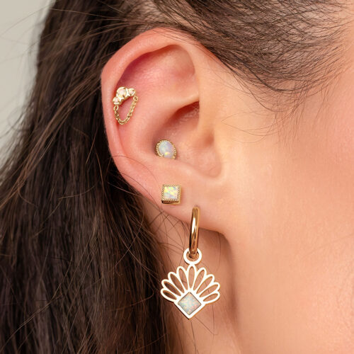 Orecchio con piercing d'oro e opale, con catena e grande orecchino pendente.