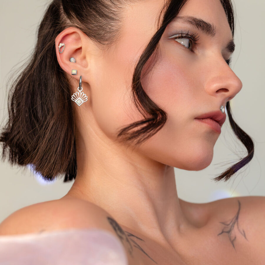 Donna con diversi piercing all'orecchio in argento, incluso un pendente a catena, su sfondo neutro