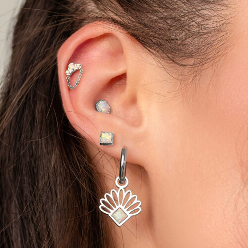 Primo piano di un orecchio con diversi piercing, incluso un piercing con opale e catena