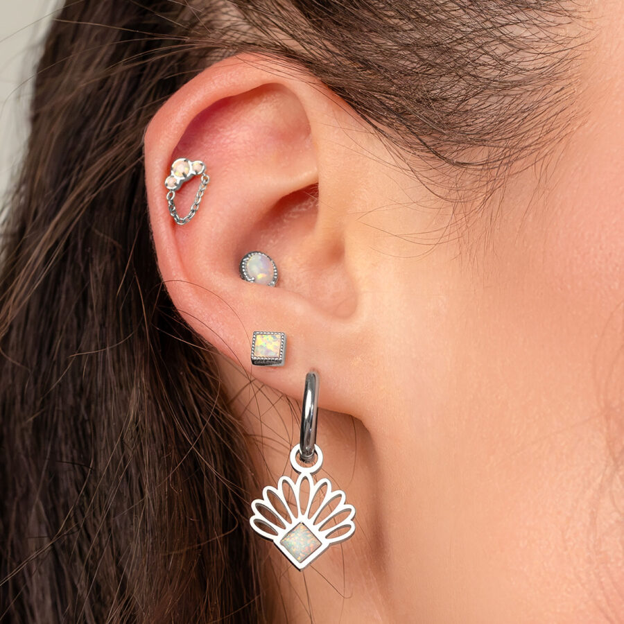 Primo piano di un orecchio con diversi piercing, incluso un piercing con opale e catena