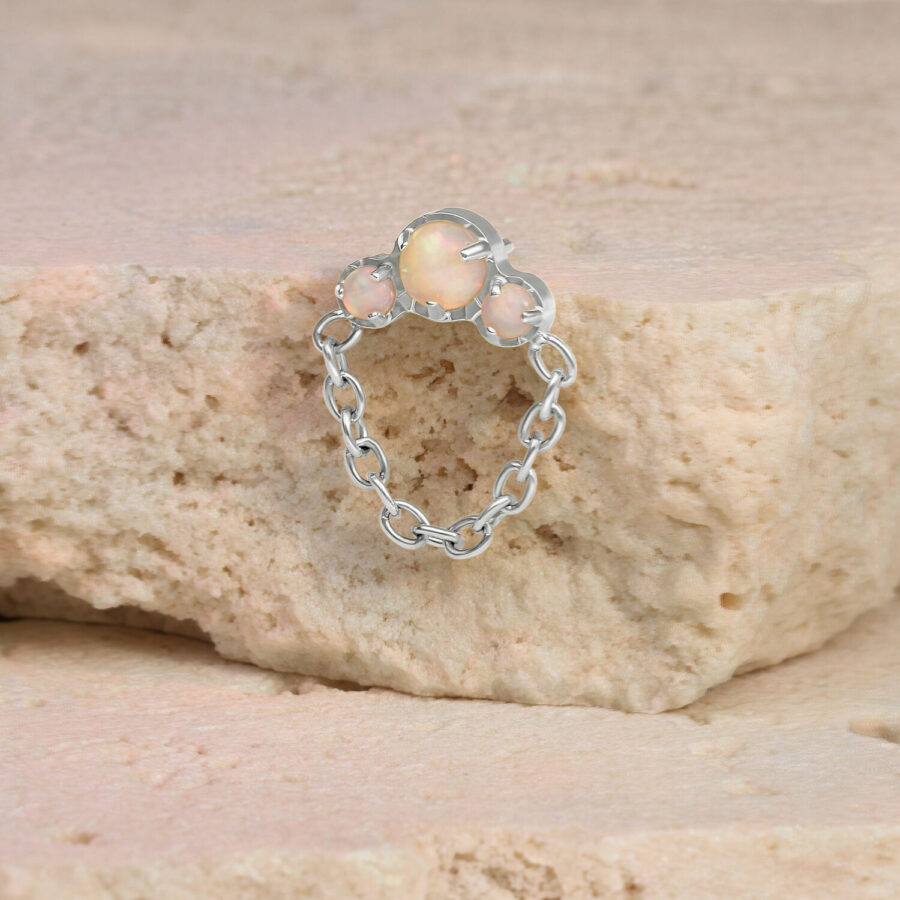 Piercing in oro bianco con opale e catena su una pietra beige