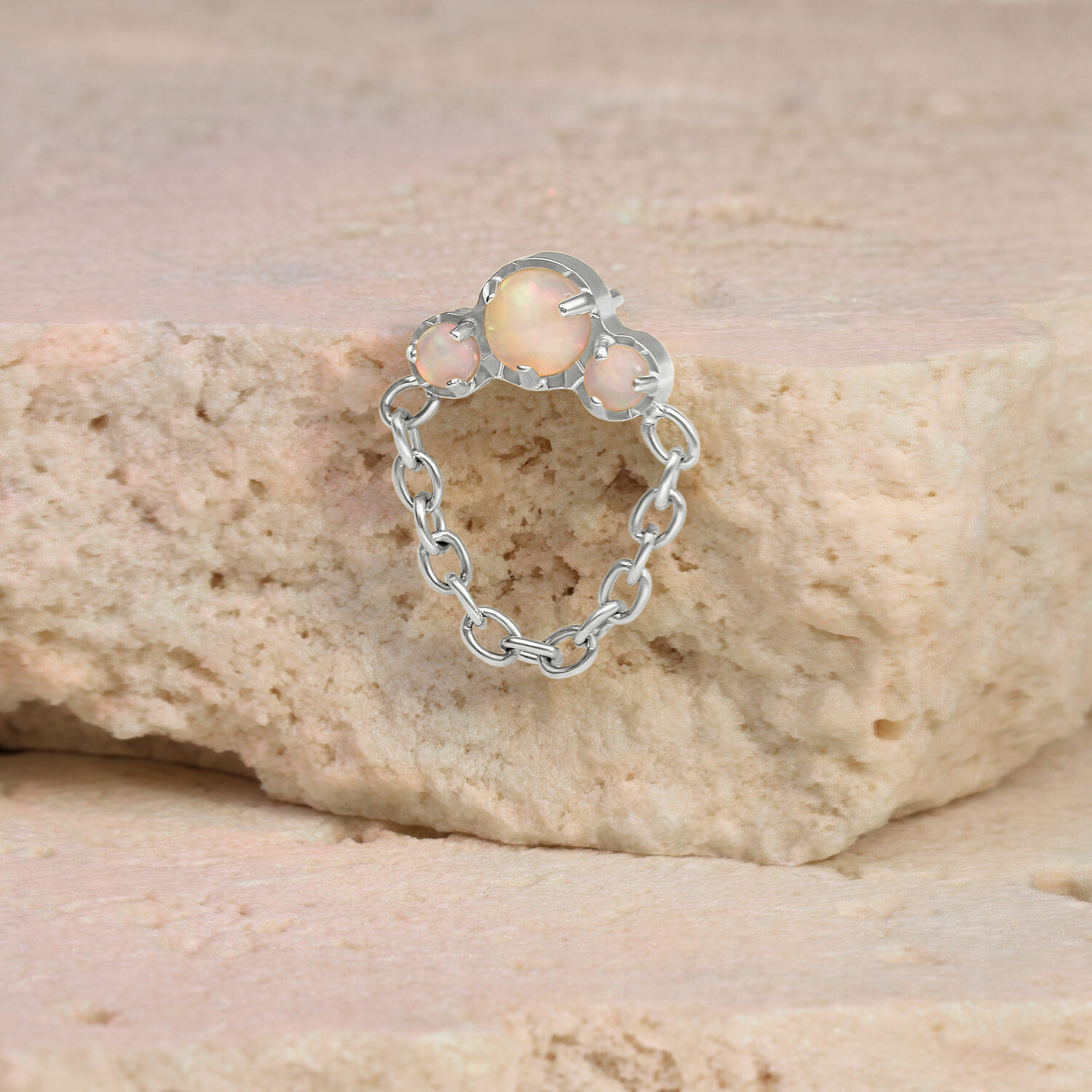 Piercing in oro bianco con opale e catena su una pietra beige