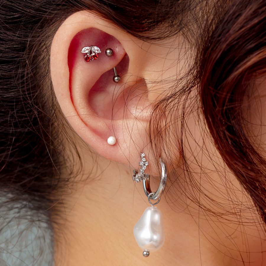Orecchio con più piercing, incluso un inserto a ciliegie argento con pietra rossa