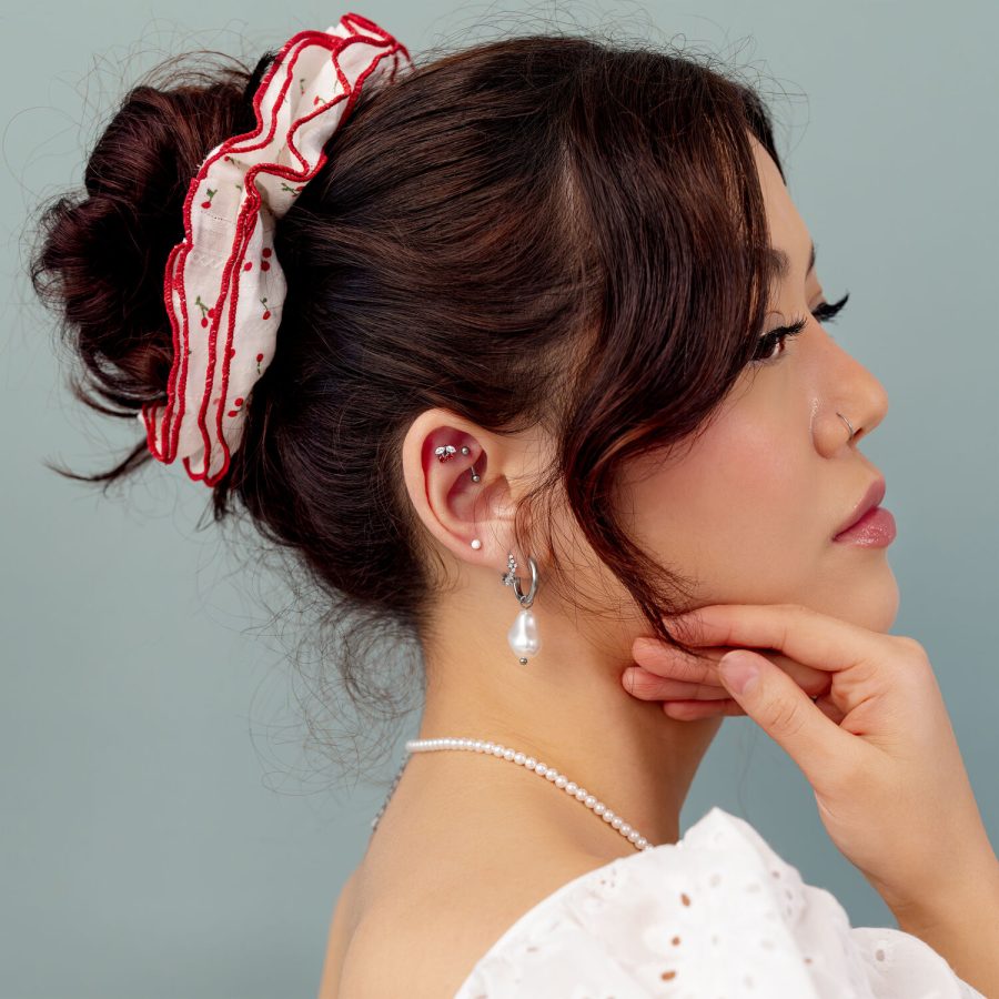 Donna con capelli raccolti, nastro rosso e orecchini di perle su sfondo grigio