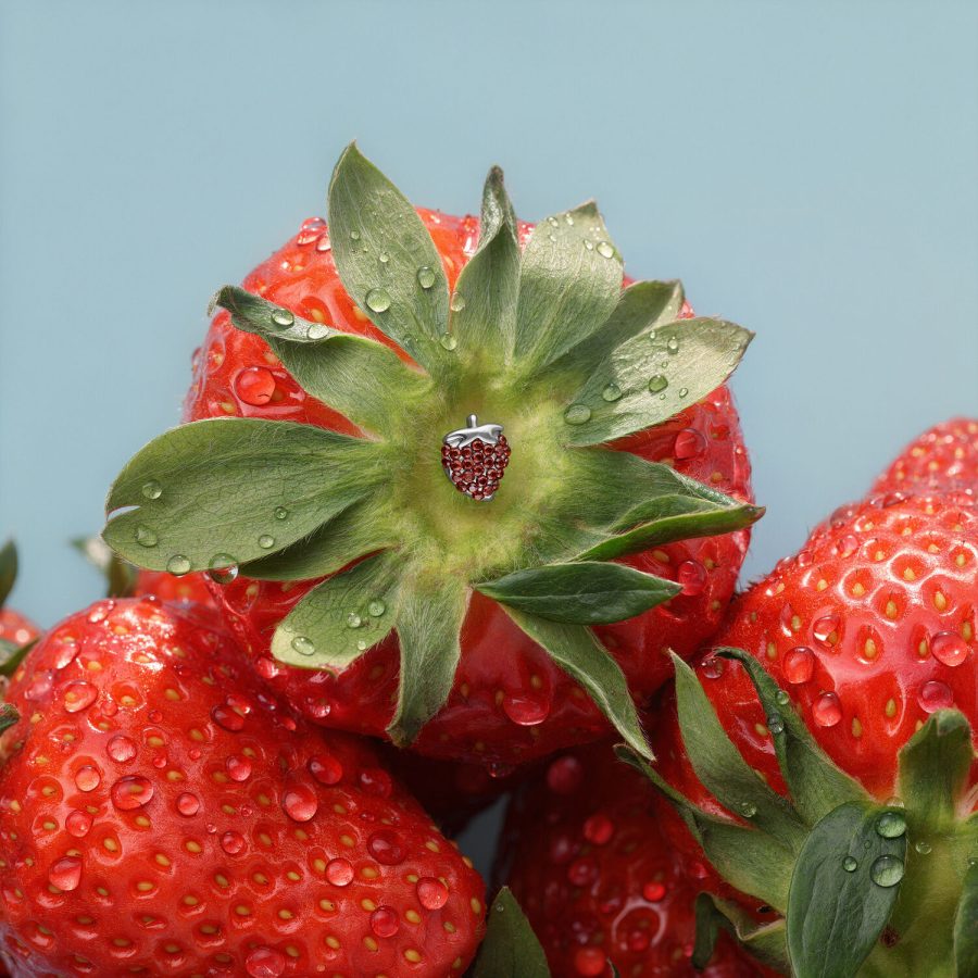 Punta a fragola argentata su una fragola rossa con gocce d'acqua su sfondo blu.