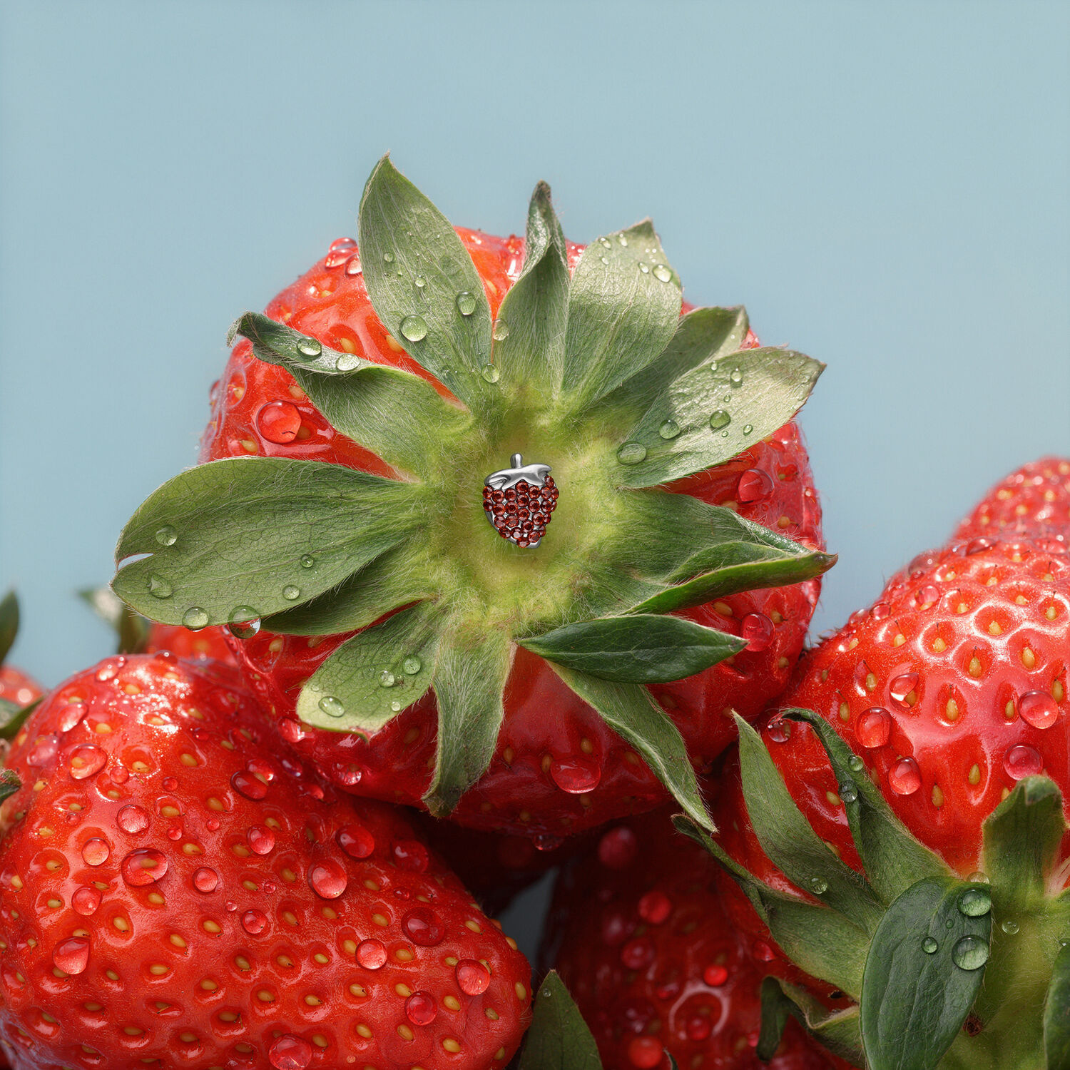 Punta a fragola in titanio per piercing Punta a fragola argentata su una fragola rossa con gocce d'acqua su sfondo blu.