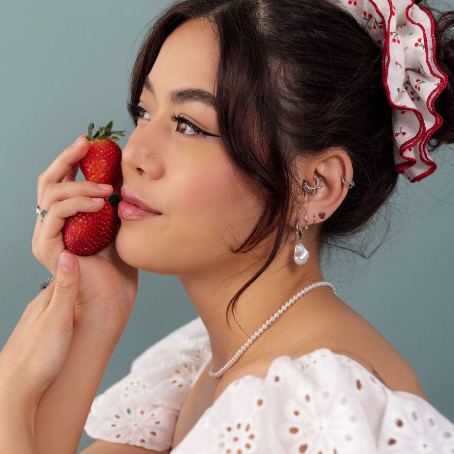 Donna con abito di pizzo bianco, fragola in mano e orecchini di gioielli su sfondo blu