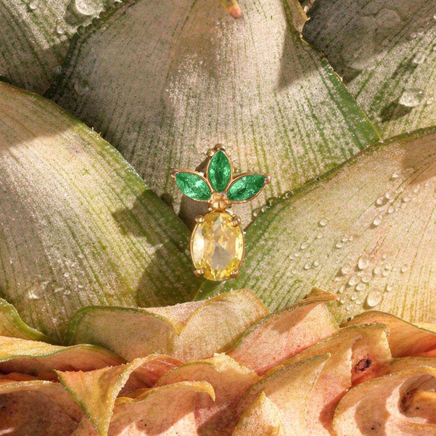 Punta per piercing ananas dorata con tre foglie verdi su buccia d'ananas