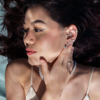 Piercing all'orecchio con attacco a tartaruga in argento Donna con diversi piercing all'orecchio in argento, incluso un attacco a tartaruga, su sfondo grigio