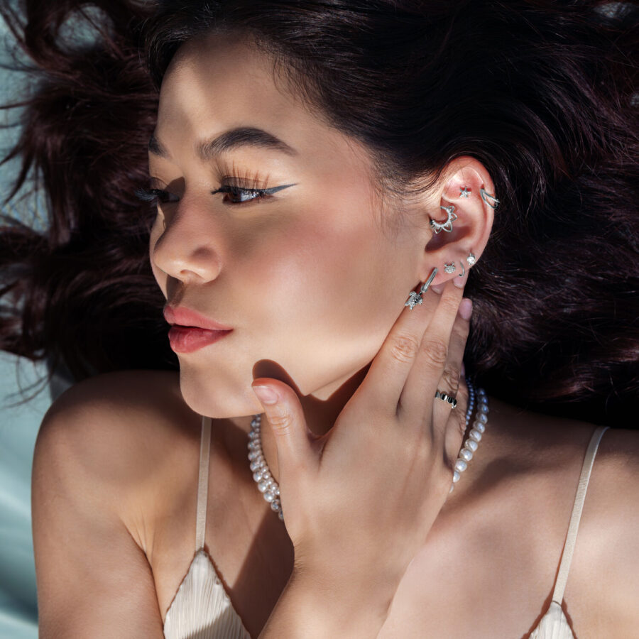 Donna con diversi piercing all'orecchio in argento, incluso un attacco a tartaruga, su sfondo grigio
