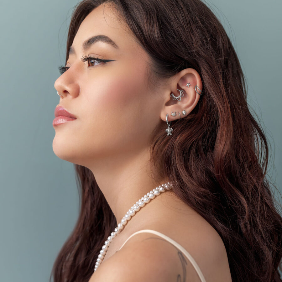 Donna con capelli castani indossa diversi piercing in argento e un ciondolo di perle su sfondo blu