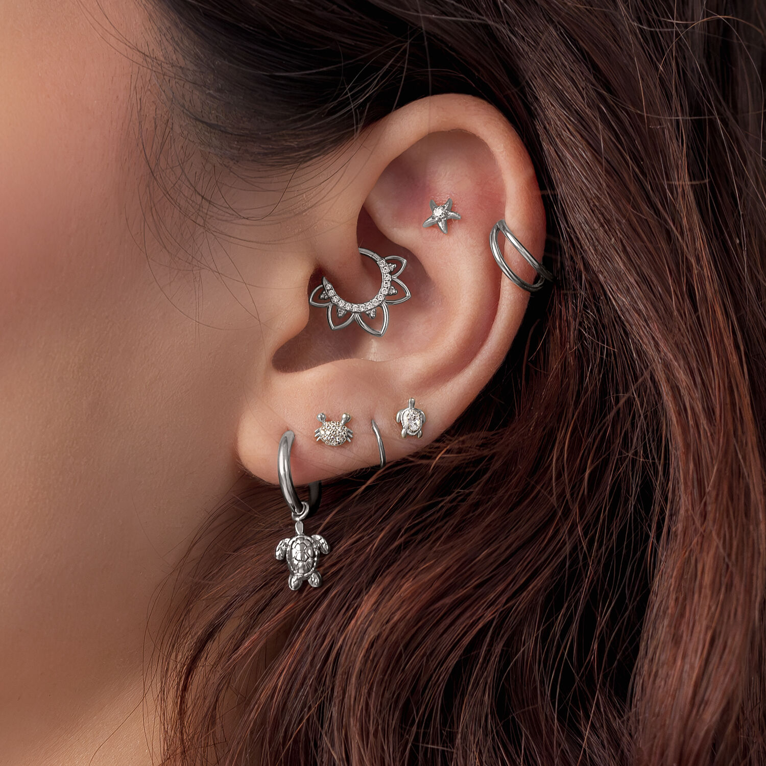 Argento Turtle Piercing per Orecchio Primo piano di un orecchio con diversi accessori per piercing in argento, incluso un motivo Turtle, su capelli castani.