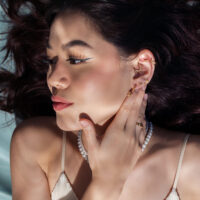 Inserto Crab dorato Push Fit all'orecchio Donna con inserti piercing dorati nell'orecchio, mano sul viso, sdraiata