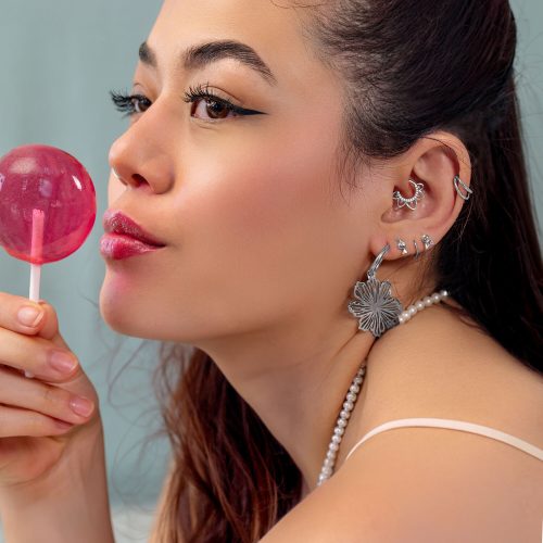 Donna con diversi orecchini a foro d'argento e un Lollipop rosa, di lato