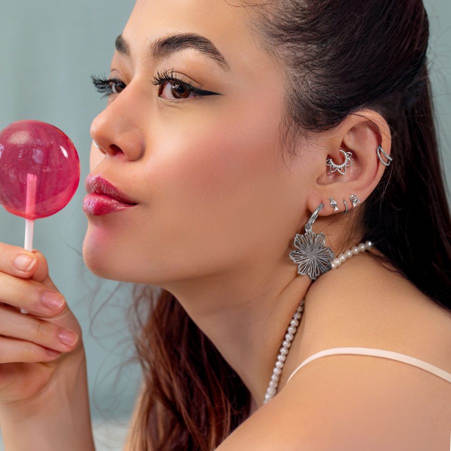 Donna con diversi orecchini a foro d'argento e un Lollipop rosa, di lato