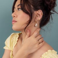 Orecchini e anelli d'oro su donna Donna con orecchini e anelli d'oro, maglia gialla, sfondo blu