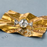 Punta per piercing a forma di caramella argento su foglio dorato con gocce d'acqua