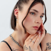 Donna con capelli corti indossa orecchini in argento e oro a forma di fungo e una collana, su sfondo bianco