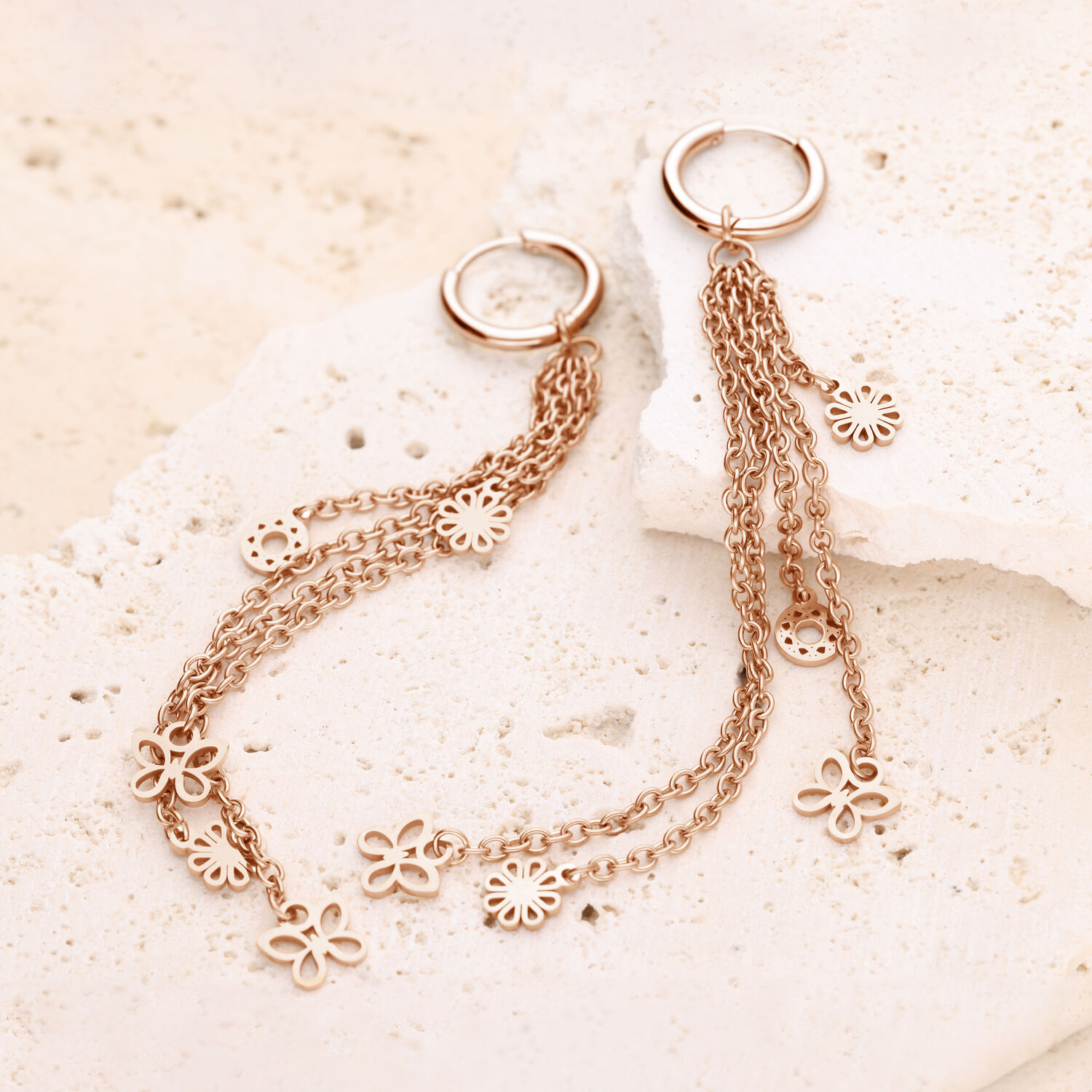 Orecchini a cerchio in oro rosa con pendenti a forma di fiore Orecchini a cerchio in oro rosa con lunghe catene e pendenti a forma di fiore su pietra chiara