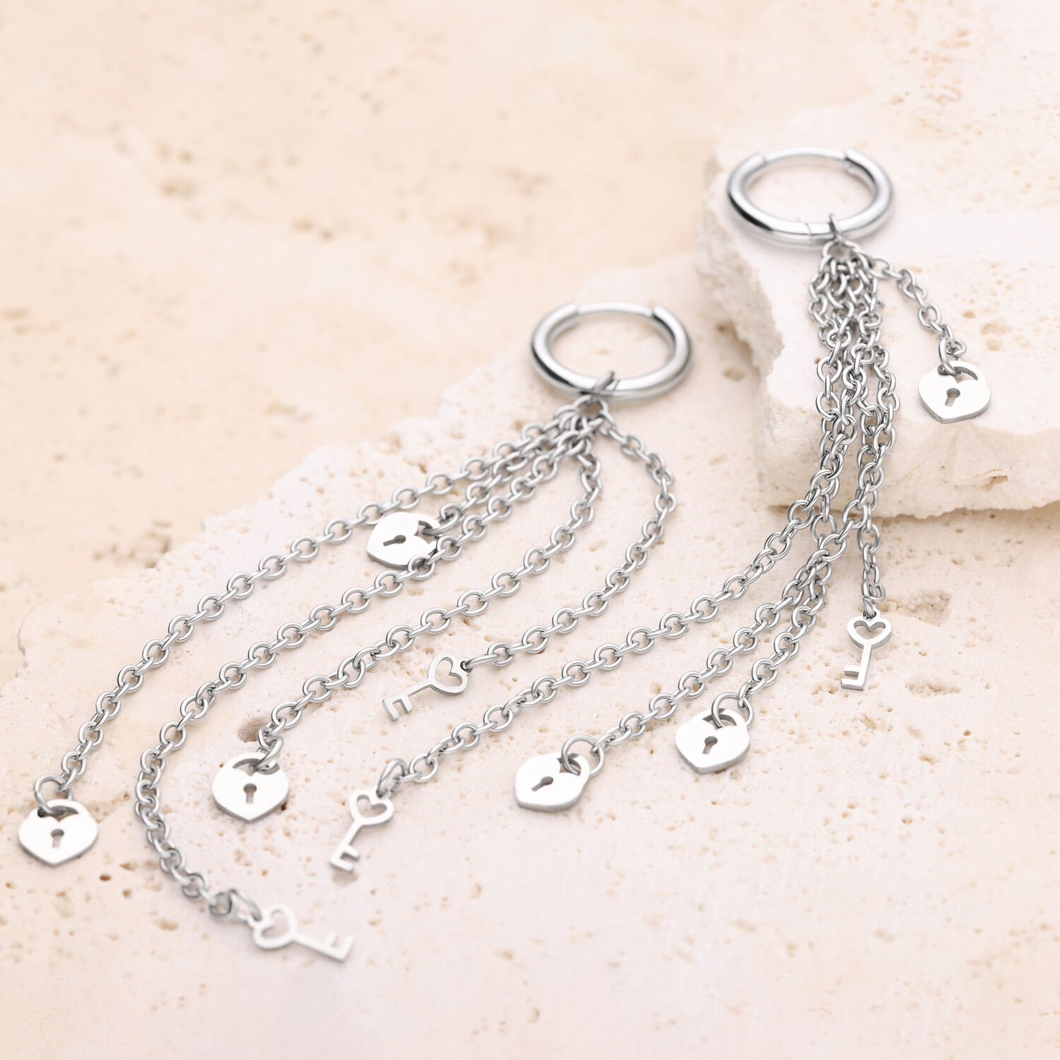 Orecchini d'argento con pendenti a catena Cerchi d'argento con lunghe catene e motivi a cuore e chiave su sfondo di pietra chiara