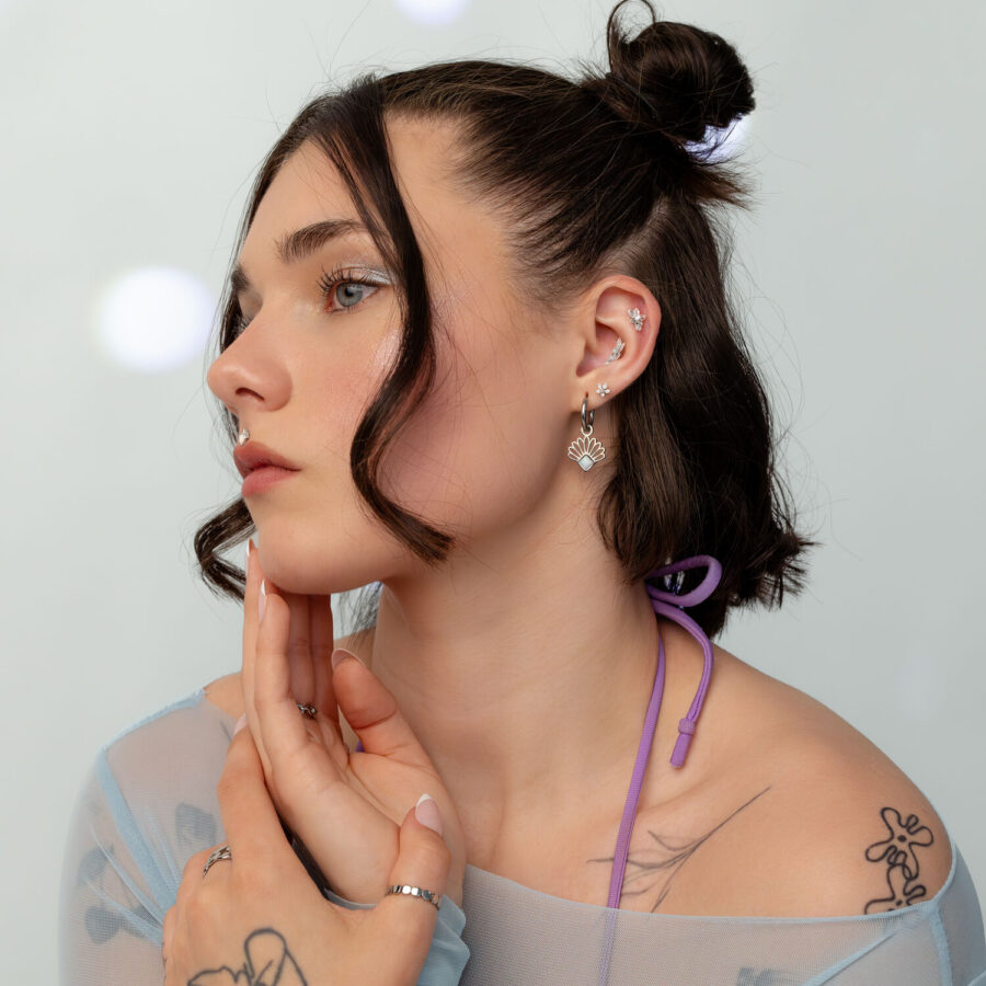 Donna con capelli scuri indossa un piercing a fiore di gelsomino in oro-bianco con opale, su sfondo chiaro