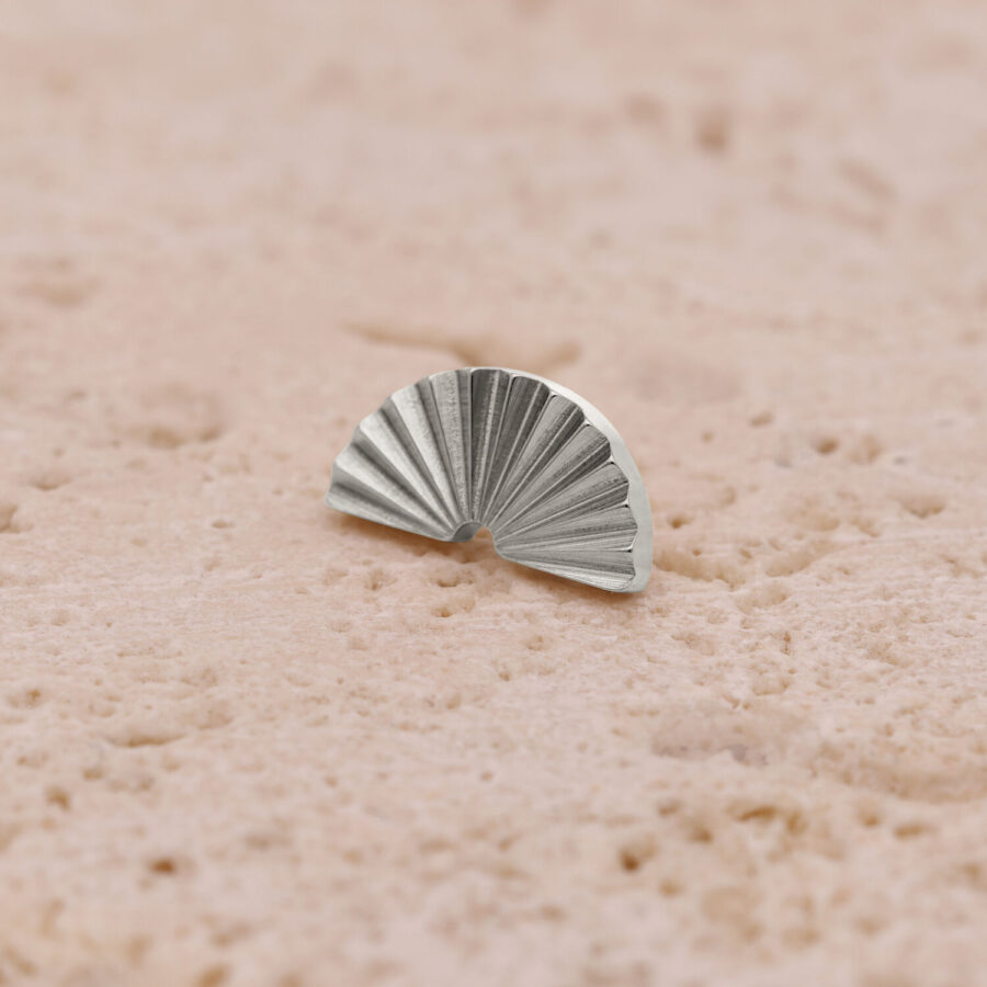 Accessorio semicircolare argentato zigrinato su superficie color sabbia
