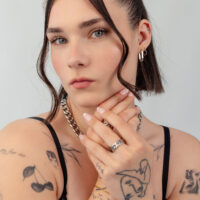 Collana e anelli d'argento con tatuaggi Donna con capelli corti, collana d'argento e diversi anelli, braccia tatuate, sfondo neutro