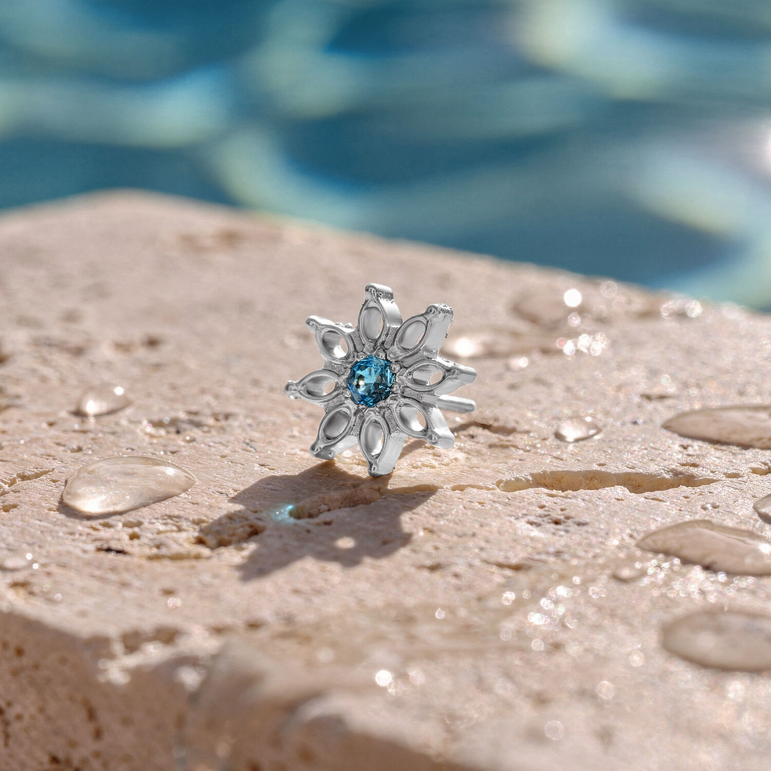 Accessorio Aqua Bloom in Cristallo Turchese Accessorio argentato con cristallo turchese su superficie di pietra bagnata davanti a uno sfondo sfocato di piscina