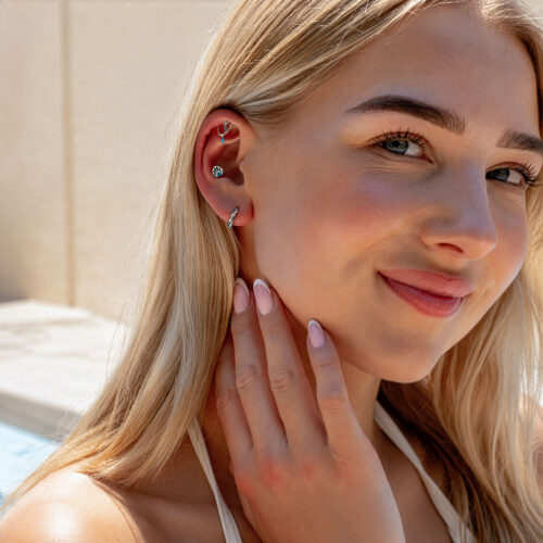 Primo piano di una donna con doppio piercing elica turchese in titanio all'orecchio, alla luce del sole