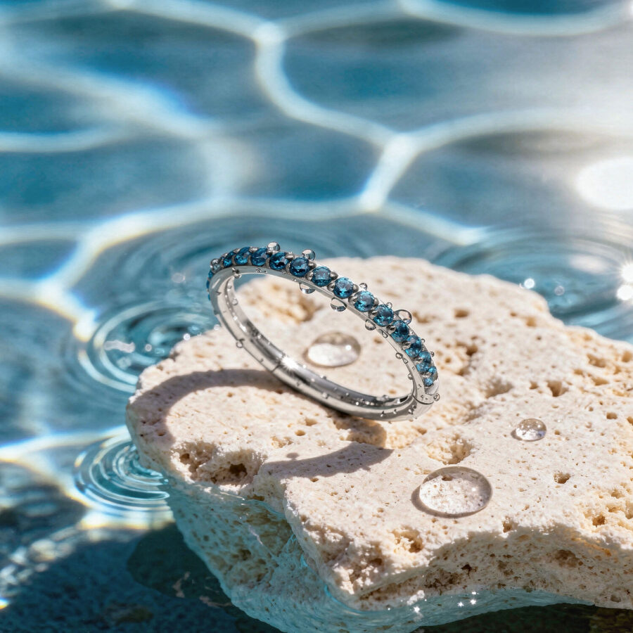 Anello di cristallo turchese su una pietra chiara al bordo di una piscina con riflessi di luce solare