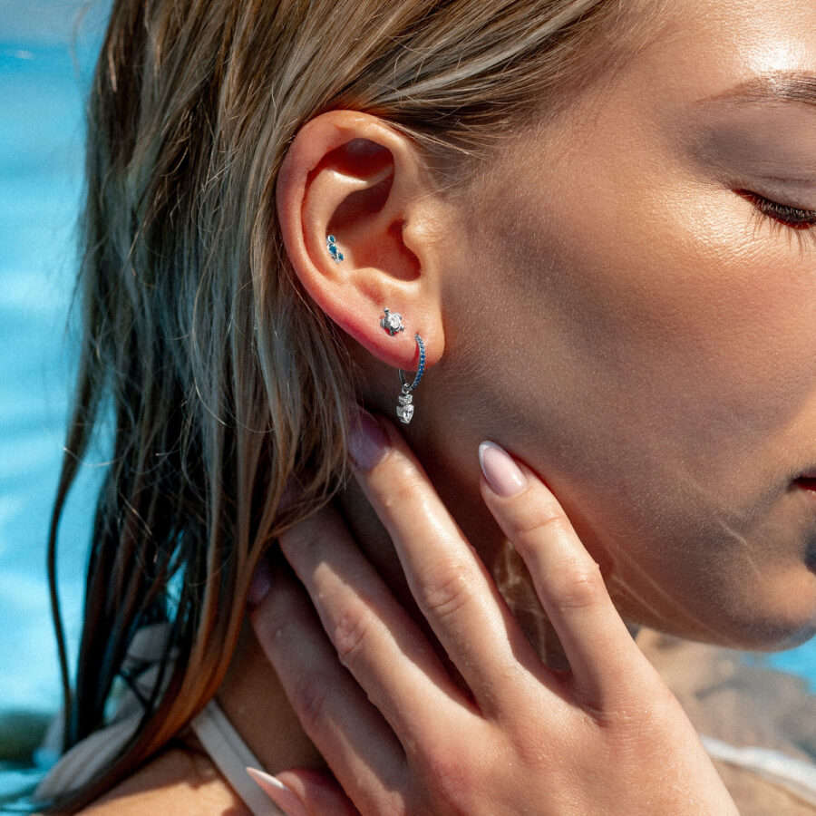 Donna con diversi piercing all'orecchio, incluso un clicker di cristallo turchese, in piscina